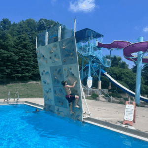 Child climbing the rock wall at Fairmont Aquatic Center, enjoying outdoor water park activities.