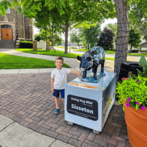 Boy standing next to a going hog wild pig statue in downtown fairmont, mn