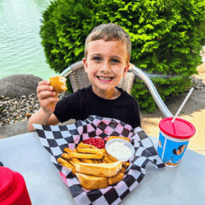 Boy sitting on the patio at The Marina Lodge in Fairmont, Minnesota, enjoying his meal with Lake Sisseton in the background