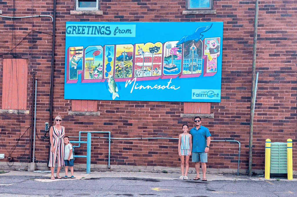 Family standing in front of the greetings from Fairmont mural in downtown fairmont, mn